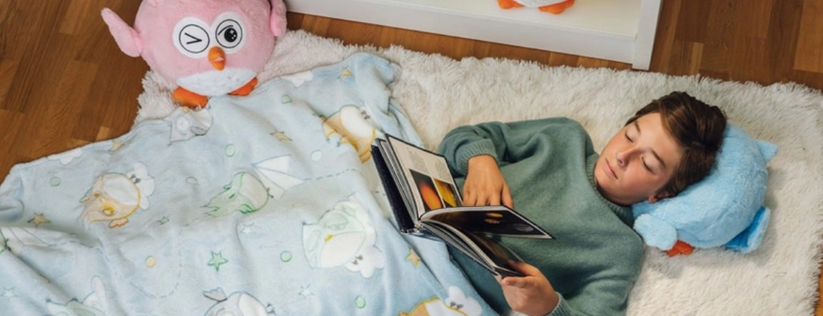 A fiú a padlón fekszik, kék takarója és két plüsse van