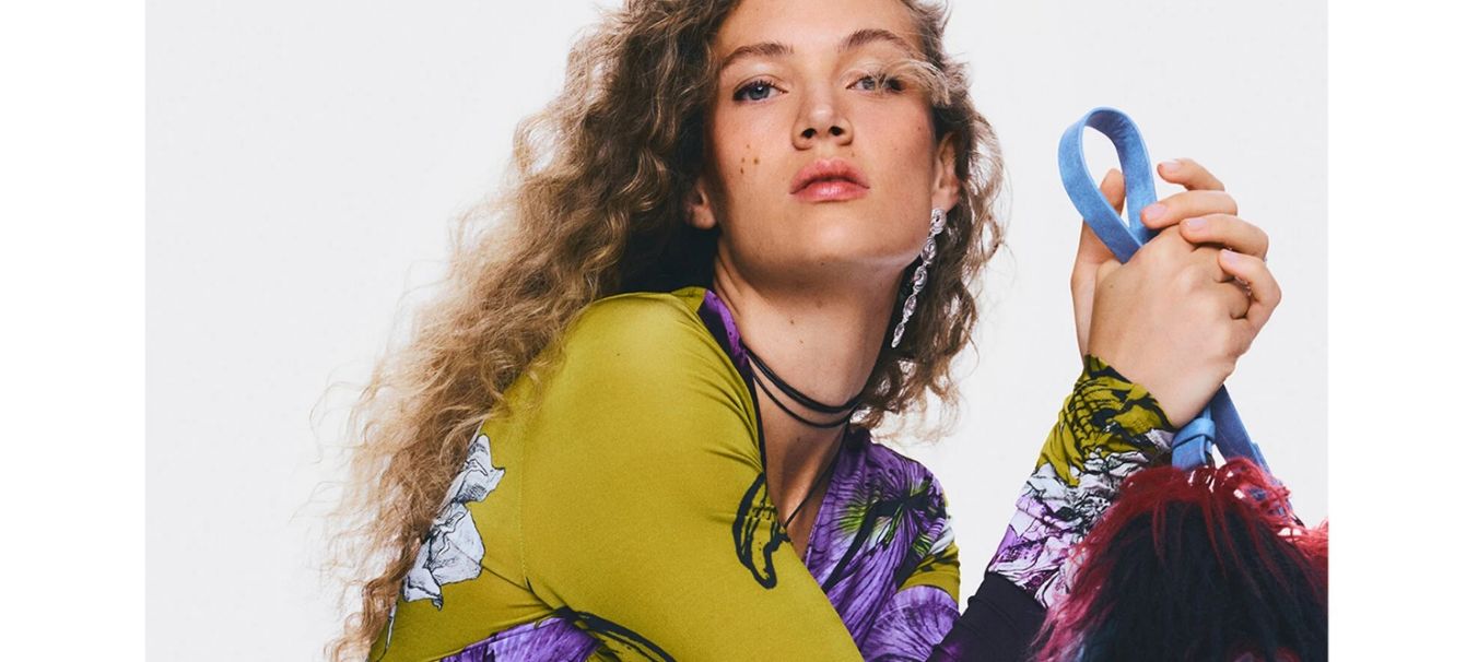 Reklámbanner, amelyen a nő desigual felsőt visel és desigual táskát tart a kezében