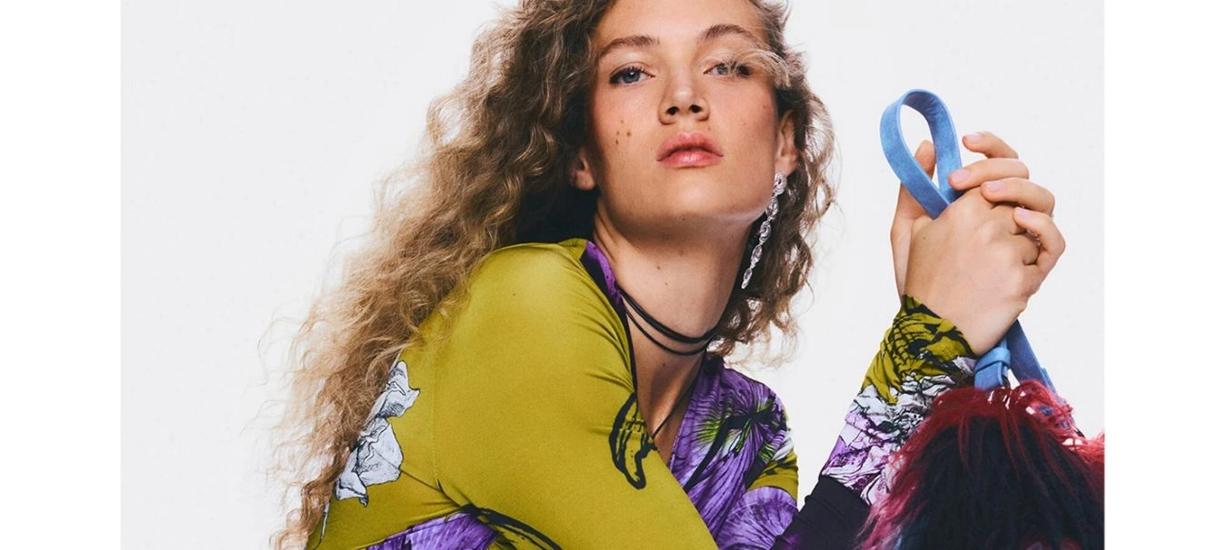 Reklámbanner, amelyen a nő desigual felsőt visel és desigual táskát tart a kezében