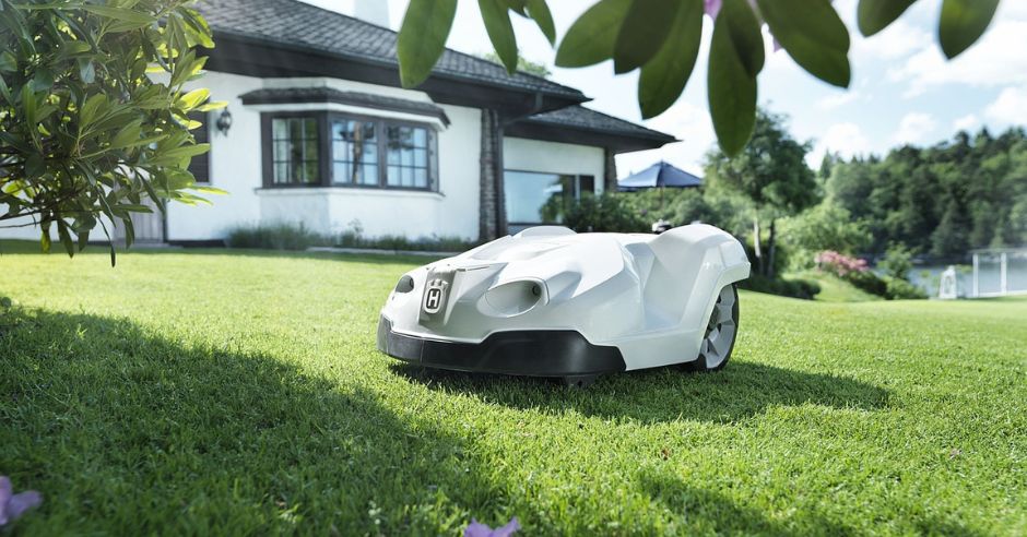 Fehér robotfűnyíró a kert zöld gyepén.
